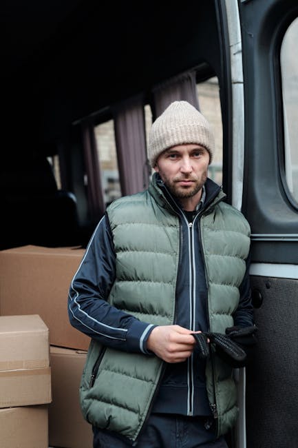 Two movers from Man and Van Swiss Cottage are engaged in a home relocation process, carefully loading a large, wrapped piece of furniture into the back of a white cargo van parked on a street. The fur