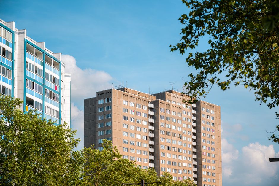A tall, multi-storey residential building constructed with reddish-brown bricks, featuring numerous small, evenly spaced white-framed windows arranged in vertical columns. The building's facade includ